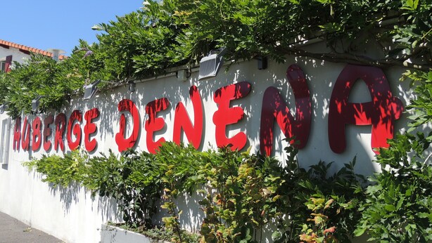 A wall with the text "HUBERGE DENEN" in large red letters, surrounded by greenery. - Auberge Denena Logis (Aicirits-Camou-Suhast)