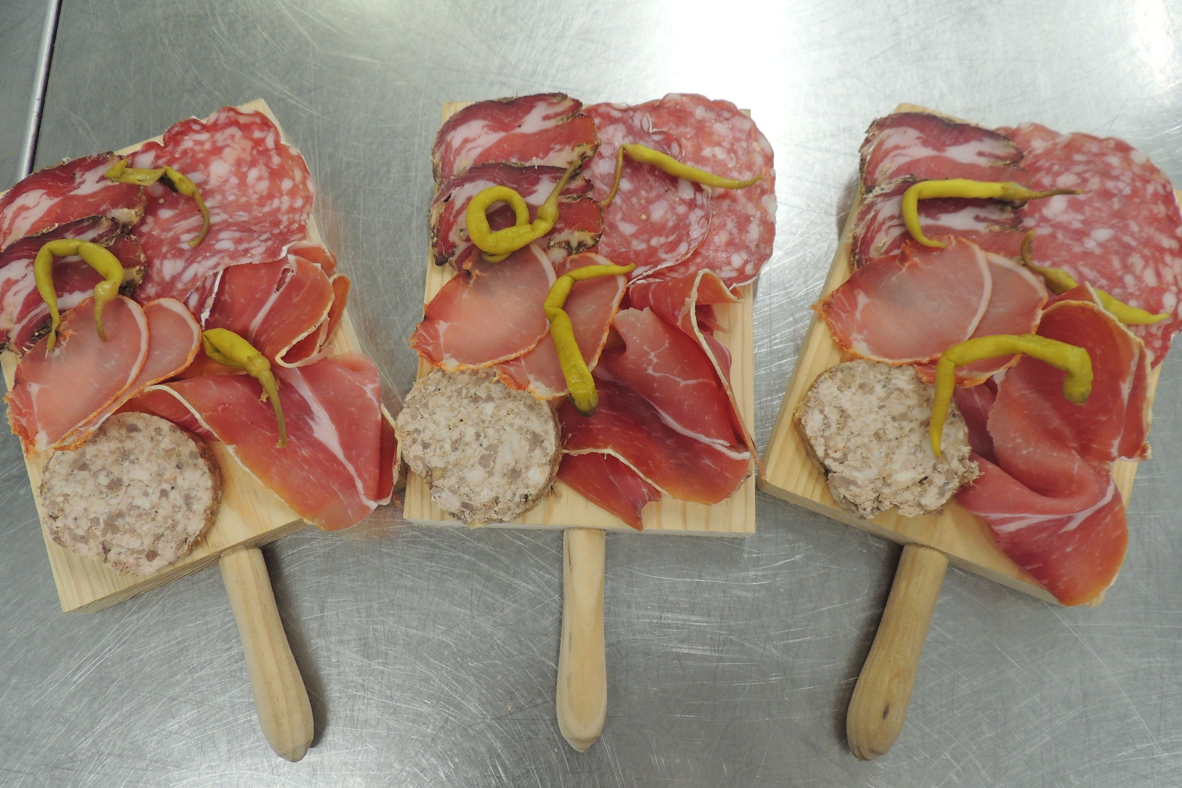 Trois planches en bois, sur lesquelles sont disposées différentes sortes de viandes et une saucisse, le tout posé sur une surface métallique.