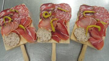 Trois planches en bois, sur lesquelles sont disposées différentes sortes de viandes et une saucisse, le tout posé sur une surface métallique.