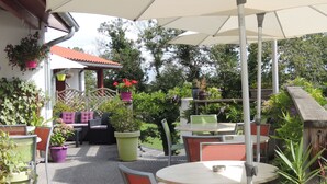 An outdoor patio area with round tables and chairs, surrounded by potted plants and a covered seating area. - Auberge Denena Logis (Aicirits-Camou-Suhast)