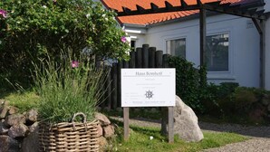Letrero de Haus Bomhoff, un jardín de casa de campo, con una cesta de mimbre y follaje en primer plano.