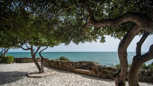 A stone-paved patio with a view of the sea, surrounded by trees and a stone wall. - Villa MG Hotel (Santa Marinella)