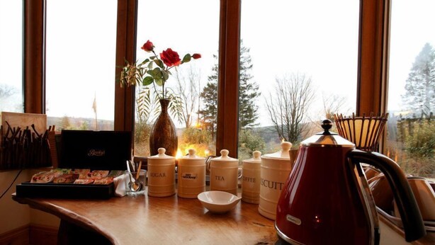 Un plan de travail de cuisine avec des récipients contenant du sucre, du thé, du café et des biscuits, une bouilloire rouge et un vase rempli de roses.
