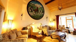 Un salon chaleureux, orné d’un grand tableau représentant un cerf, avec des poutres en bois au plafond et un mélange de meubles rembourrés à motifs floraux et unis.