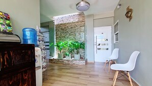 Amplia sala de estar con una pared de acento de piedra, un dispensador de agua y dos sillas blancas.