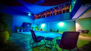 Un área de piscina exterior moderna con una estructura de dos niveles, zonas de estar e iluminación ambiental.
