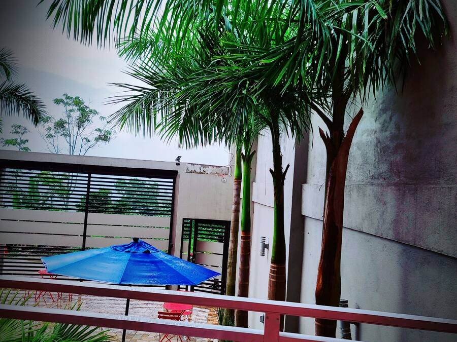 Un balcón con vista a un patio, que incluye una sombrilla azul y mobiliario de exterior.