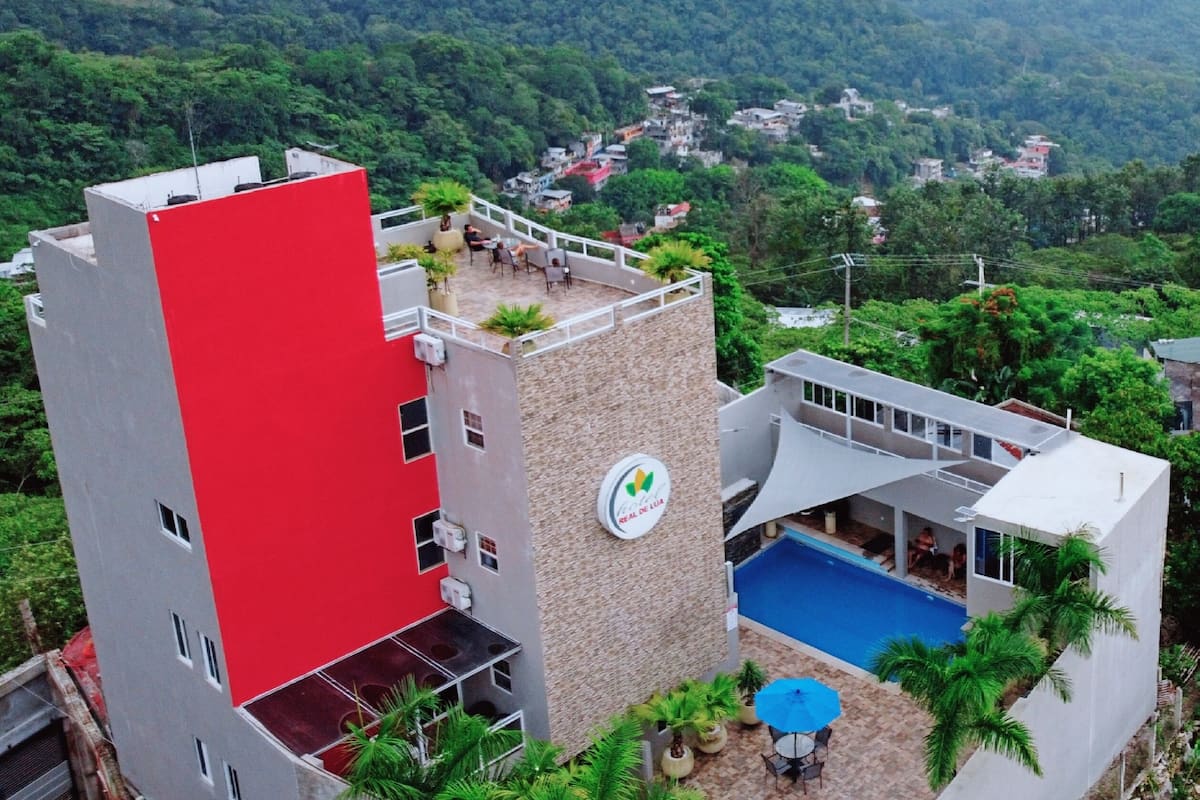 Um edifício moderno com uma seção vermelha, uma piscina e vista para uma paisagem verde exuberante.