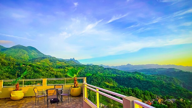 Una terraza con vistas a un valle exuberante y montañas distantes, con plantas en macetas y mobiliario de exterior.