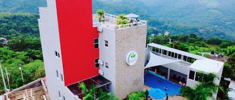 Un hotel con un edificio rojo y blanco, una piscina y vistas al entorno verde.