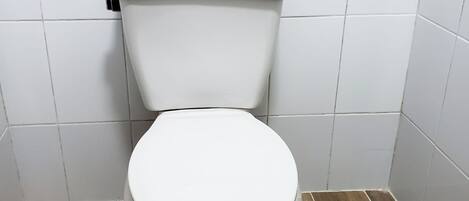 A toilet in a bathroom with white tiles on the walls and a wooden floor.