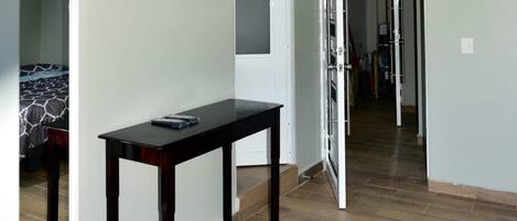 A hallway with a wooden floor, a black table with a remote control, and a TV mounted on the wall.