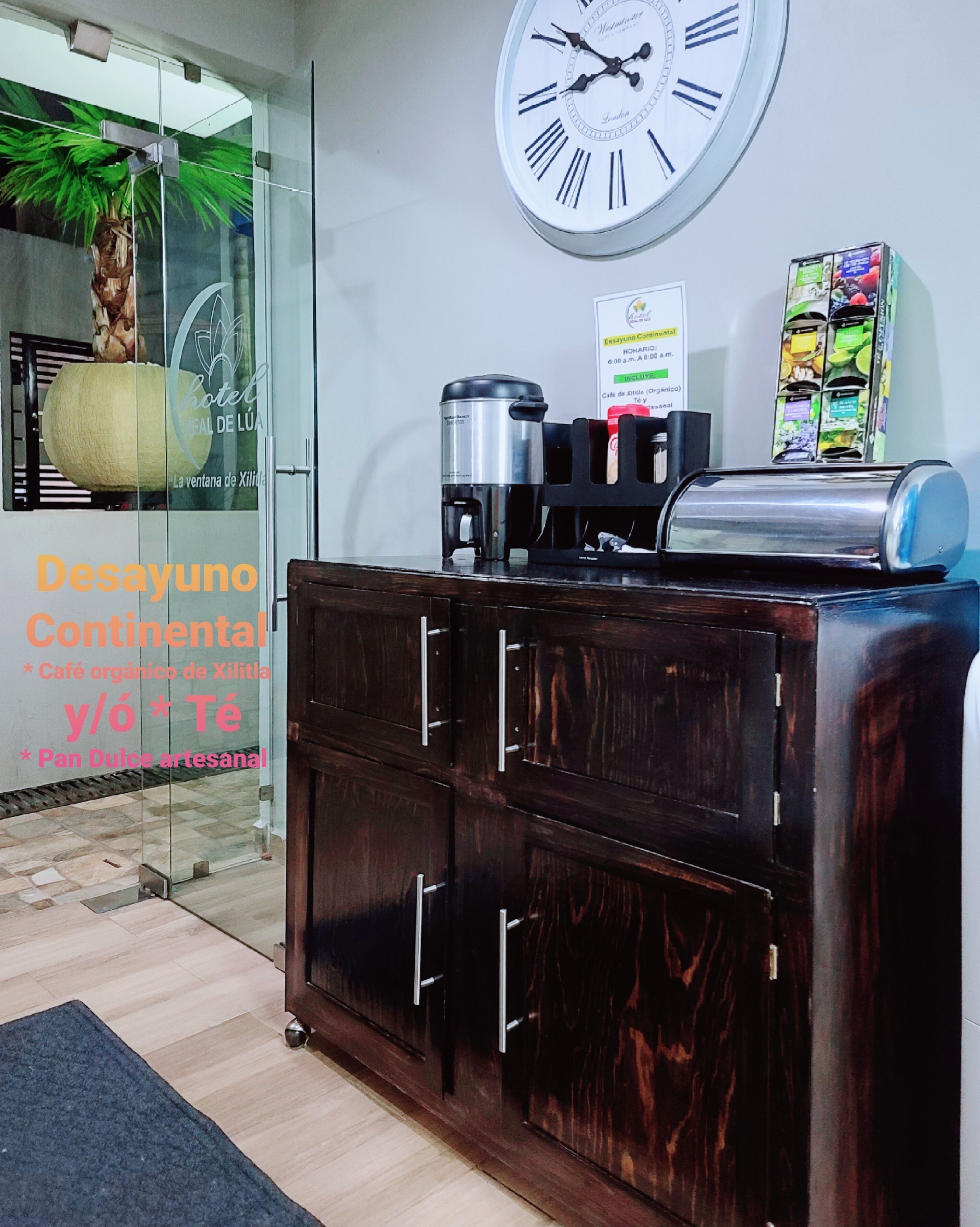 A reception area with a clock, a coffee machine, and a sign indicating continental breakfast.