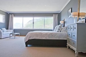 A bedroom with a large bed, a dresser, a nightstand, and a window with curtains.