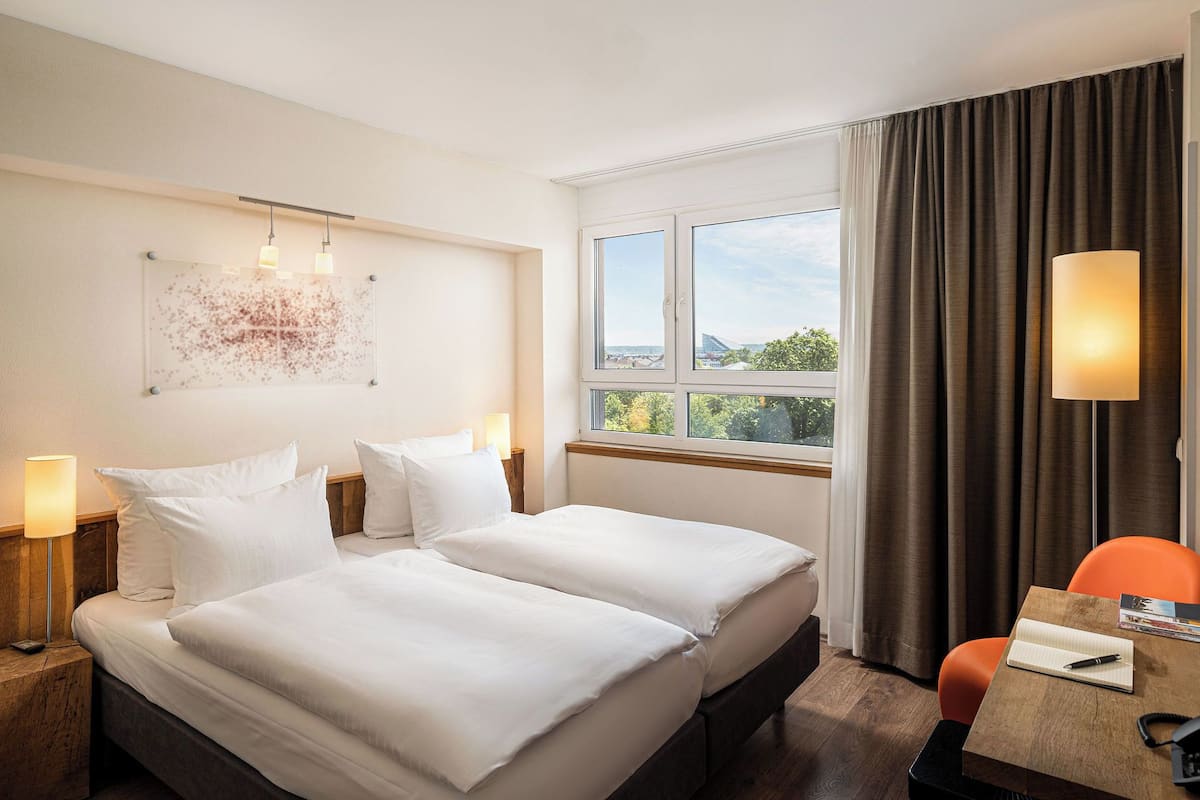 Habitación de hotel con dos camas, un escritorio, una silla, un televisor y una ventana con cortinas.