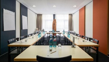 Una sala conferenze con lunghe tavolate, sedie e una grande scultura in legno al centro.