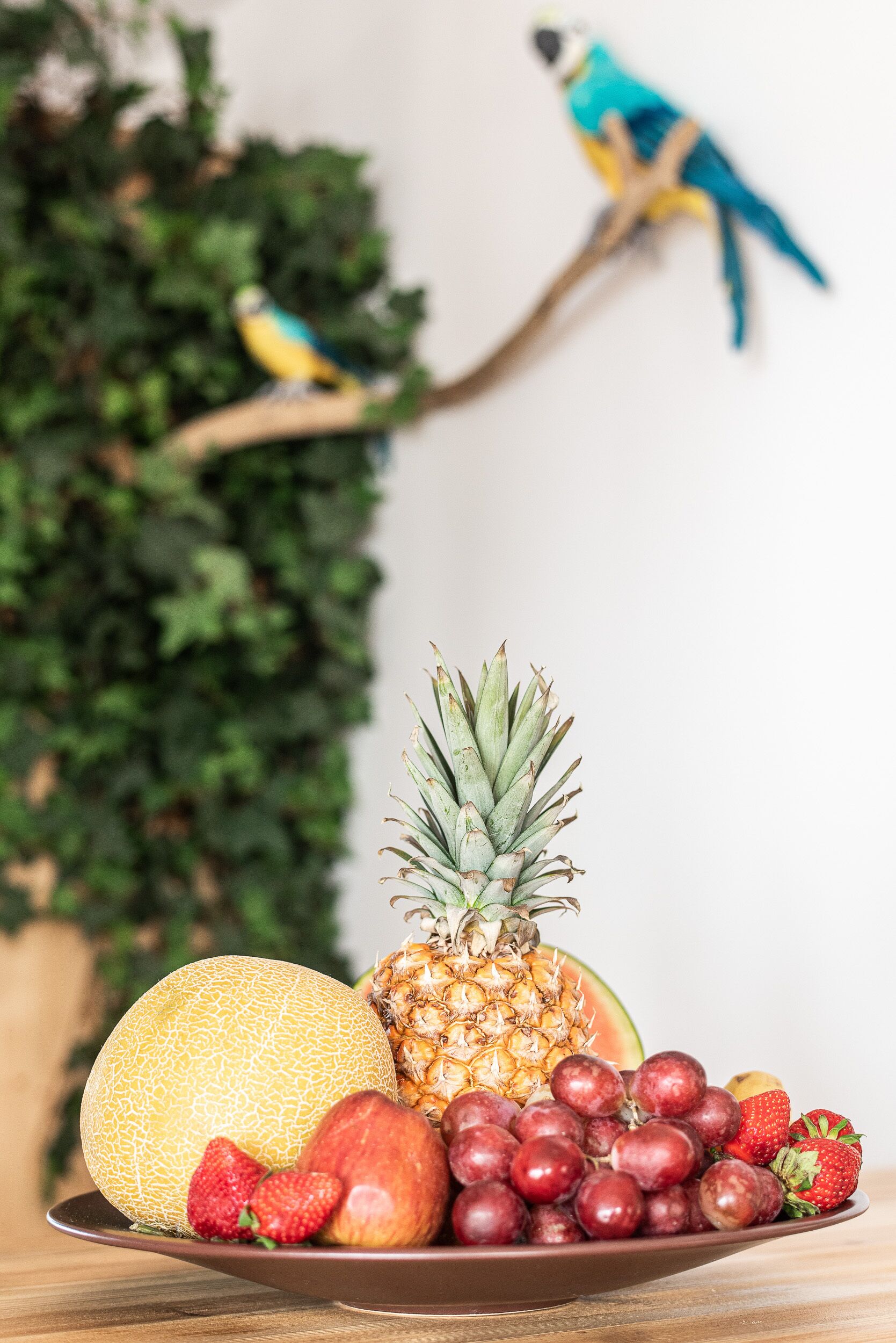 Une assiette contenant un ananas, un melon, des fraises et des raisins.