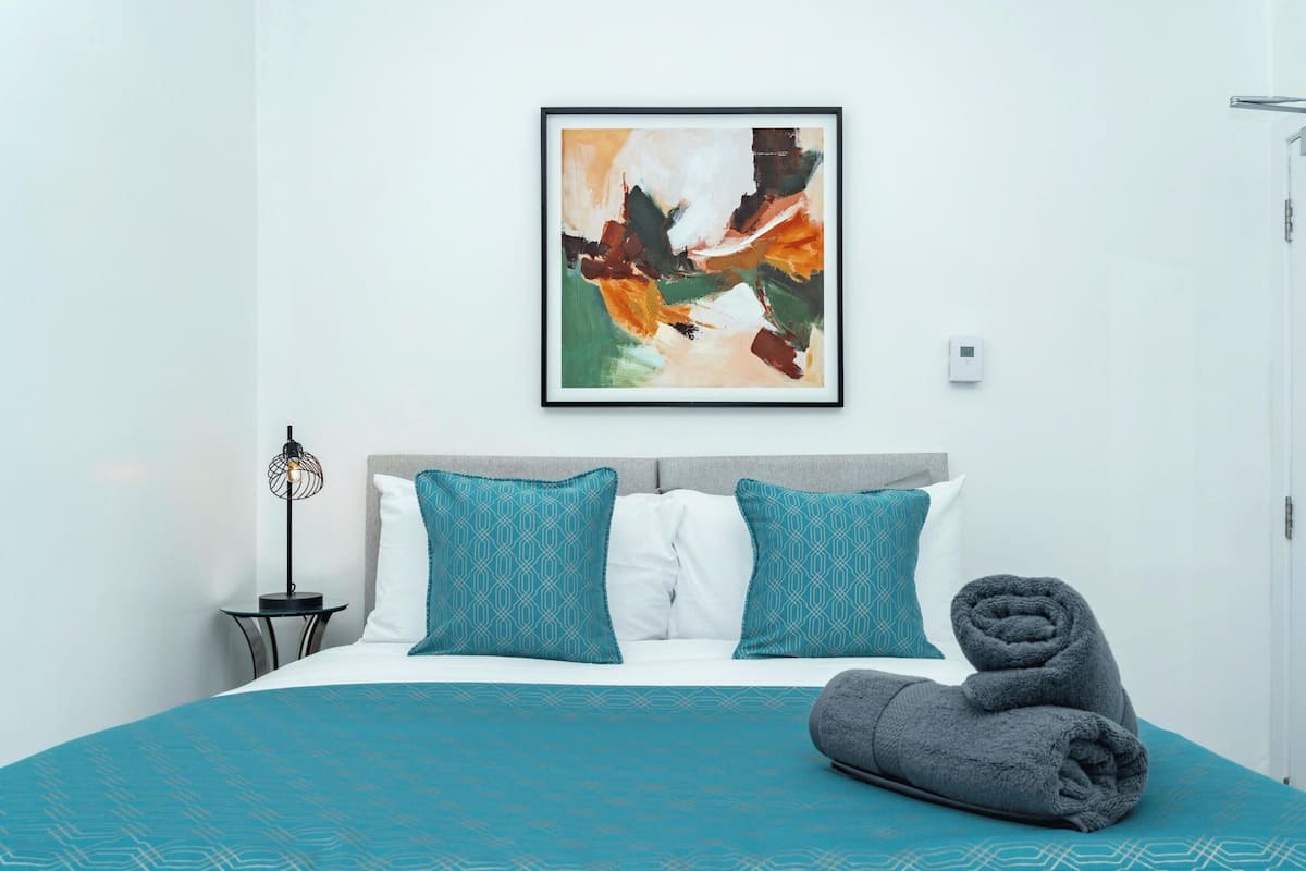 A neatly made bed with a teal patterned bedspread, two teal pillows, and a rolled gray towel.