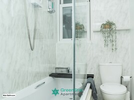 A main bathroom with a glass-enclosed shower, a white toilet, and a shelf with toiletries.