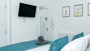 A modern bedroom with a bed, a flat-screen TV, a door with a sign, and framed artwork on the wall.