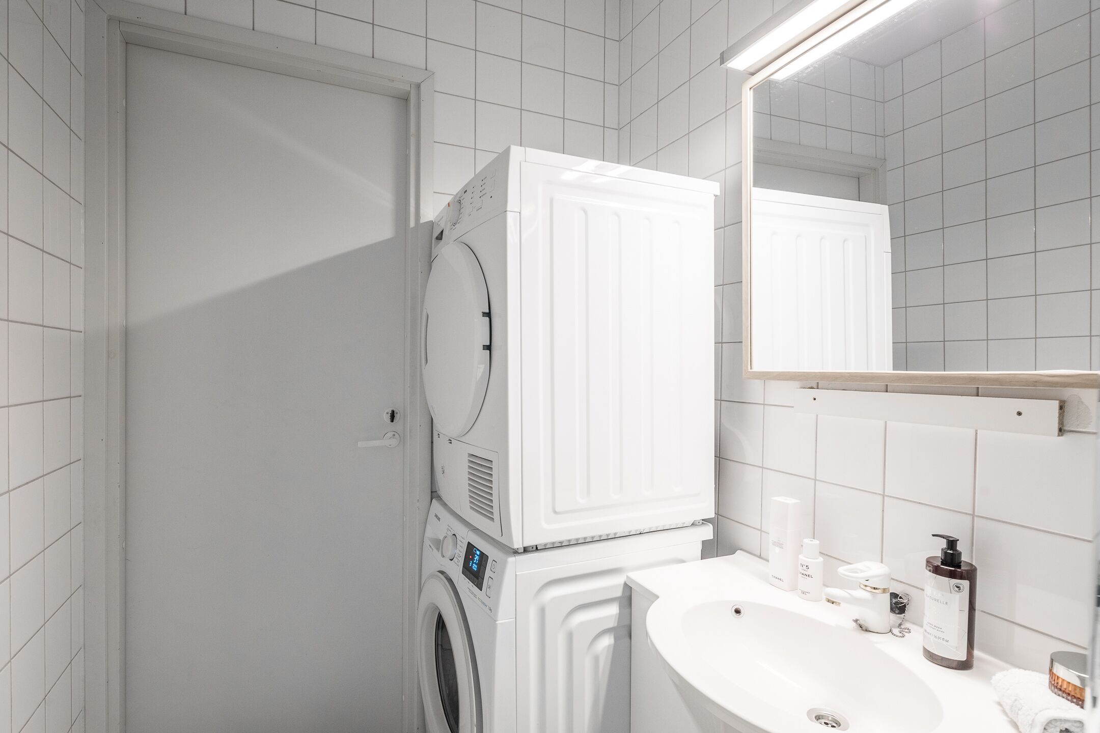 Een moderne badkamer met een witte wasmachine, een wastafel met toiletartikelen en een spiegel.