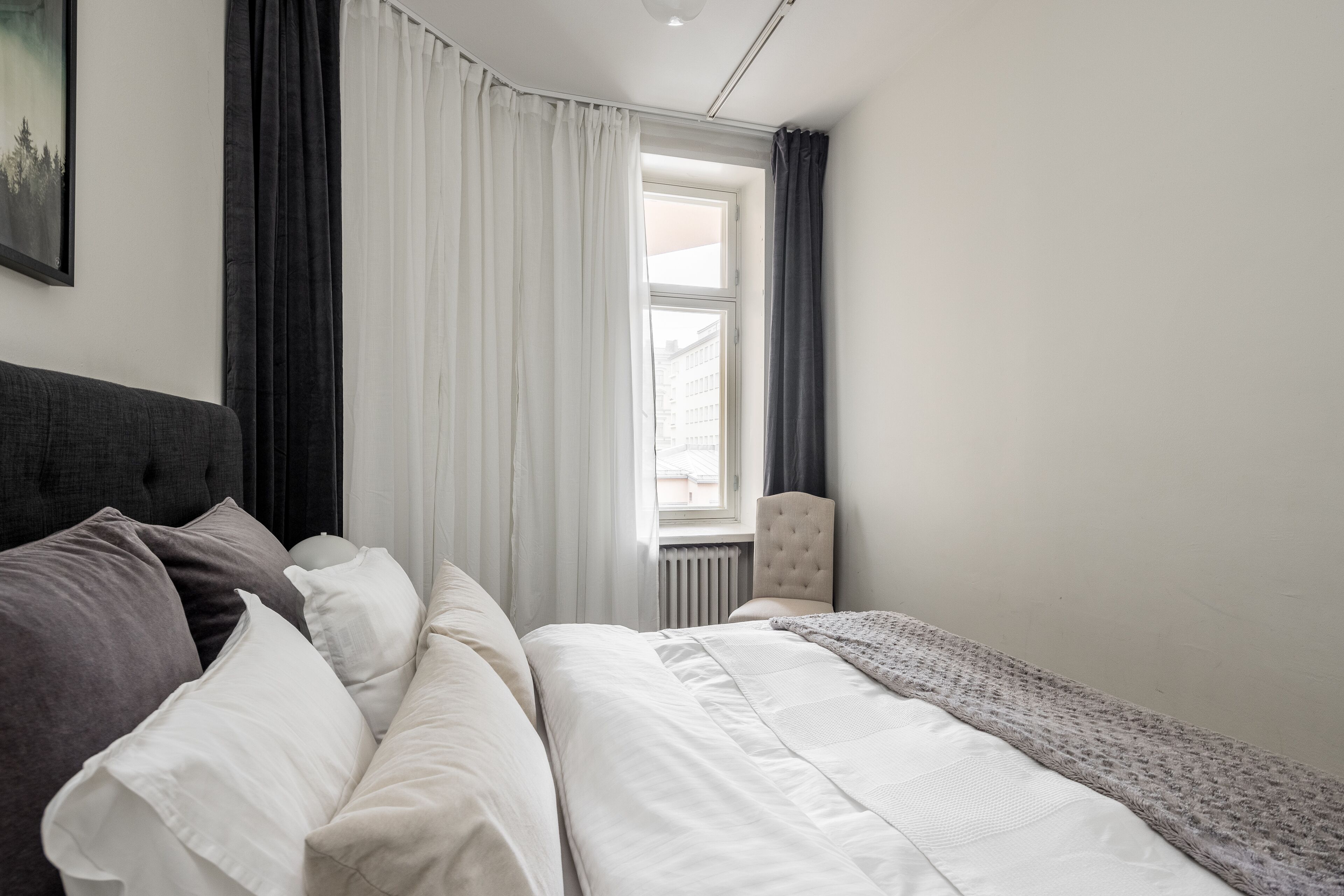 A bedroom with a bed, a chair, and a window with curtains.