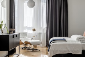 A modern hotel room with a bed, a desk, a chair, and a lamp.