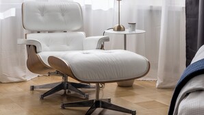 Ein modernes Zimmer mit einem weißen Ledersessel, einem kleinen runden Tisch mit einer Lampe und transparenten Vorhängen.