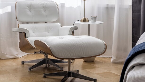 Una habitación moderna con un sillón de cuero blanco, una mesita redonda con una lámpara y cortinas de gasa.