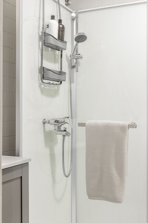 A shower with a handheld showerhead, a wall-mounted faucet, and a towel rack with a towel.