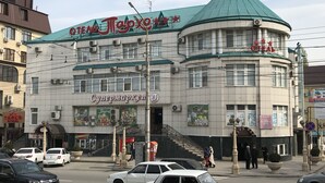 Un edificio con techo verde y varios letreros, incluyendo uno para un supermercado y otro para un bar.