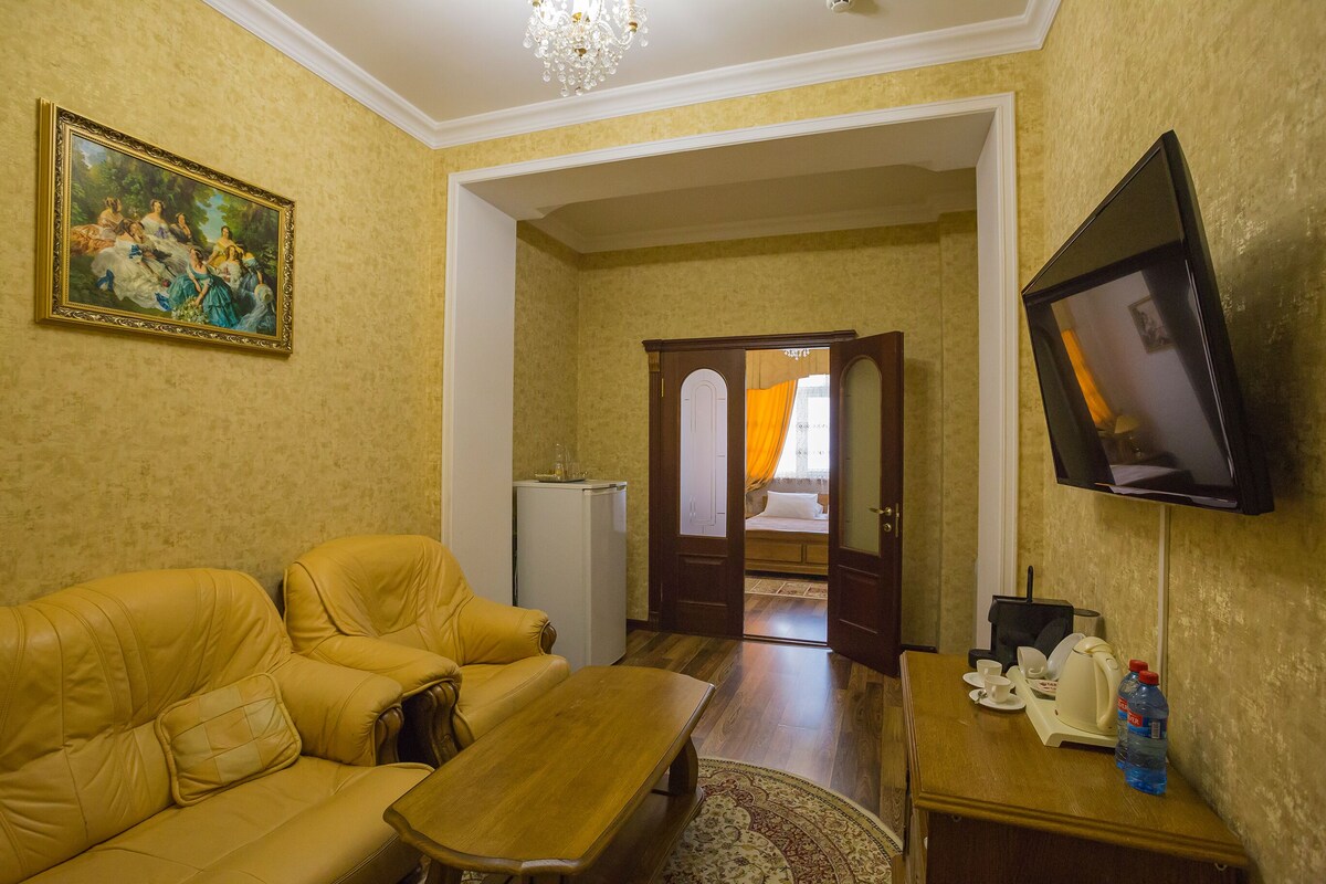 Una sala de estar con sofá, mesa de centro y televisor. Hay un cuadro en la pared y una puerta que conduce a otra habitación.