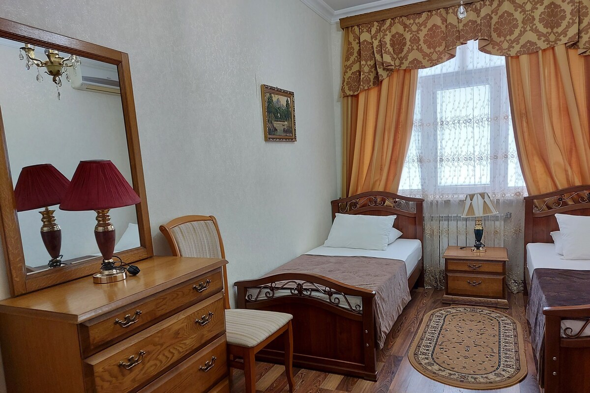 Un dormitorio con cama de madera, mesita de noche, cómoda, silla y ventana con cortinas.
