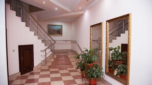 Vestíbulo de hotel con suelo de cuadros, una escalera con barandillas metálicas y plantas en macetas.