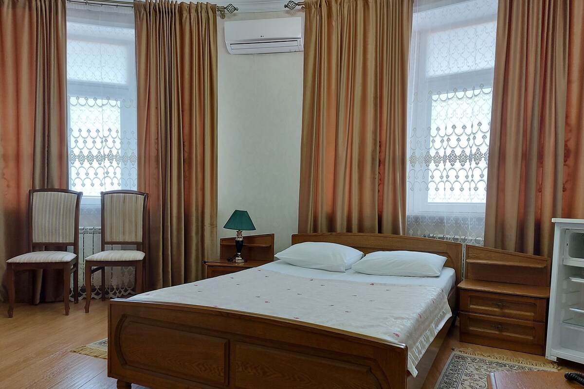 Un dormitorio con una cama de madera, dos sillas, una mesita de noche con lámpara y un aparador.