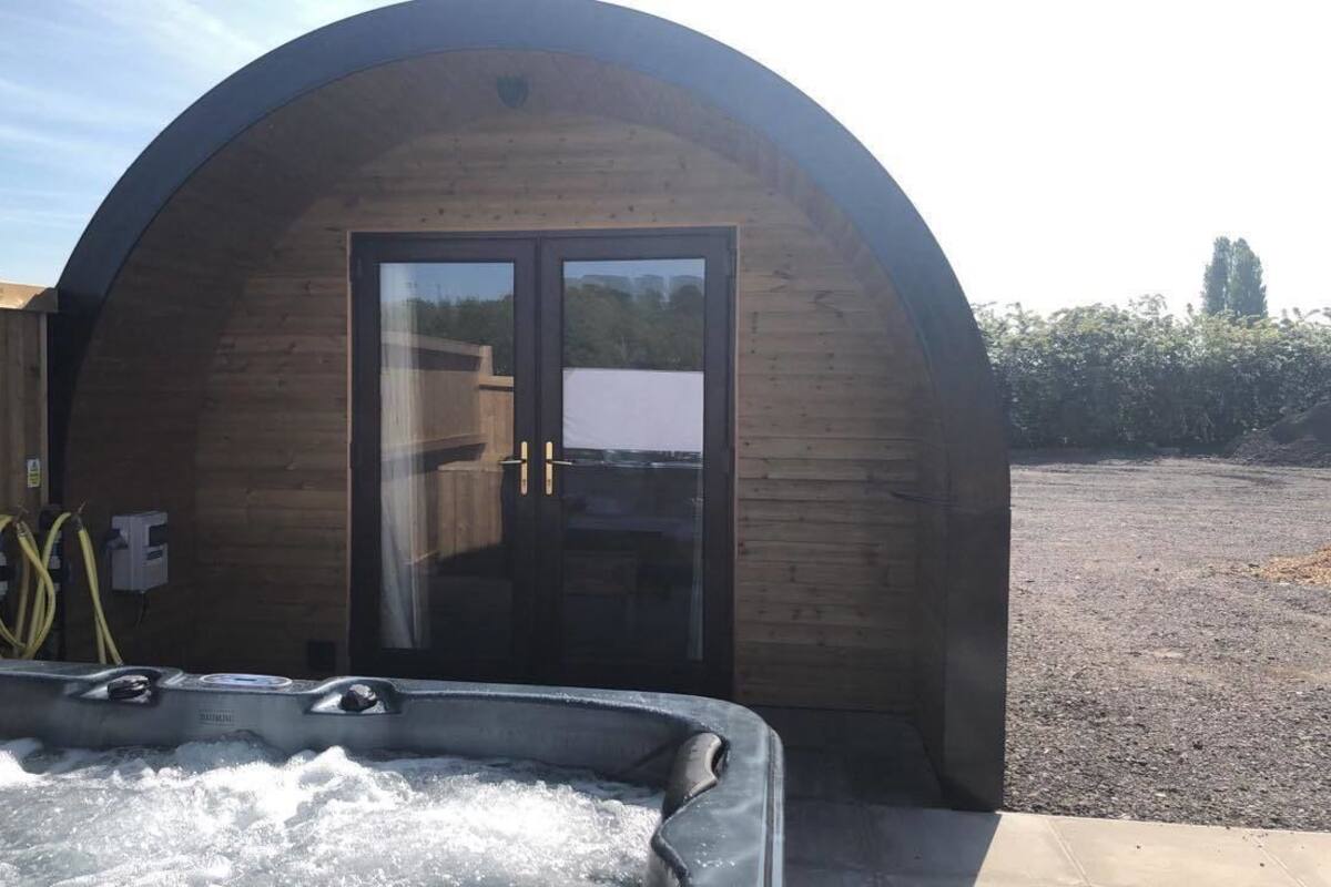 A wooden structure with a glass door, a hot tub in front, and a wooden fence in the background.