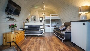 A compact room with a bunk bed, a desk, a sofa, a TV mounted on the wall, and a lamp. - Cheshire Glamping Pods (Frodsham)