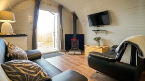 A cozy living room with a fireplace, a flat-screen TV, and a sofa with patterned cushions. - Cheshire Glamping Pods (Frodsham)