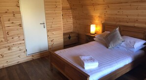 Habitació d'una cabana de fusta amb un llit, una meseta de nit amb una làmpada i un armari.