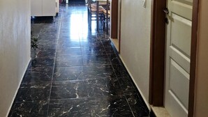 Un pasillo con piso de mármol, un comedor con mesa y sillas, una zona de cocina con armarios y estantes, y una puerta con la etiqueta 'WC BAYAN'.