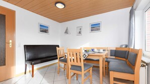 Un área de comedor con un sofá negro, sillas de madera y una mesa con un periódico.