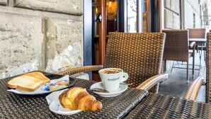 Una silla de mimbre con un plato de croissants y tostadas, una taza de café y un pequeño bol de yogur.