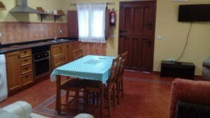 Una cucina compatta con mobili in legno, un tavolo da pranzo con sedie, un estintore e un televisore fissato alla parete.