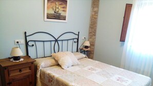 Un letto rifatto con una coperta a fiori, un comodino in legno con una lampada e una colonna in pietra.
