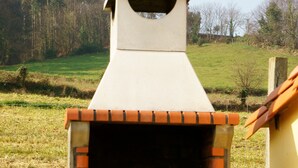 Un forno in mattoni con camino, situato in un prato erboso con alberi sullo sfondo.