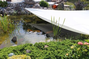 Uno stagno con rocce, piante e una tenda bianca.