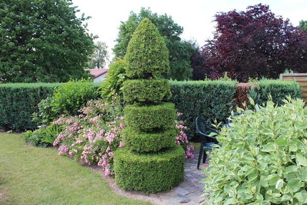 Un jardín con setos cuidadosamente podados, una topiary de varios niveles y plantas con flores.