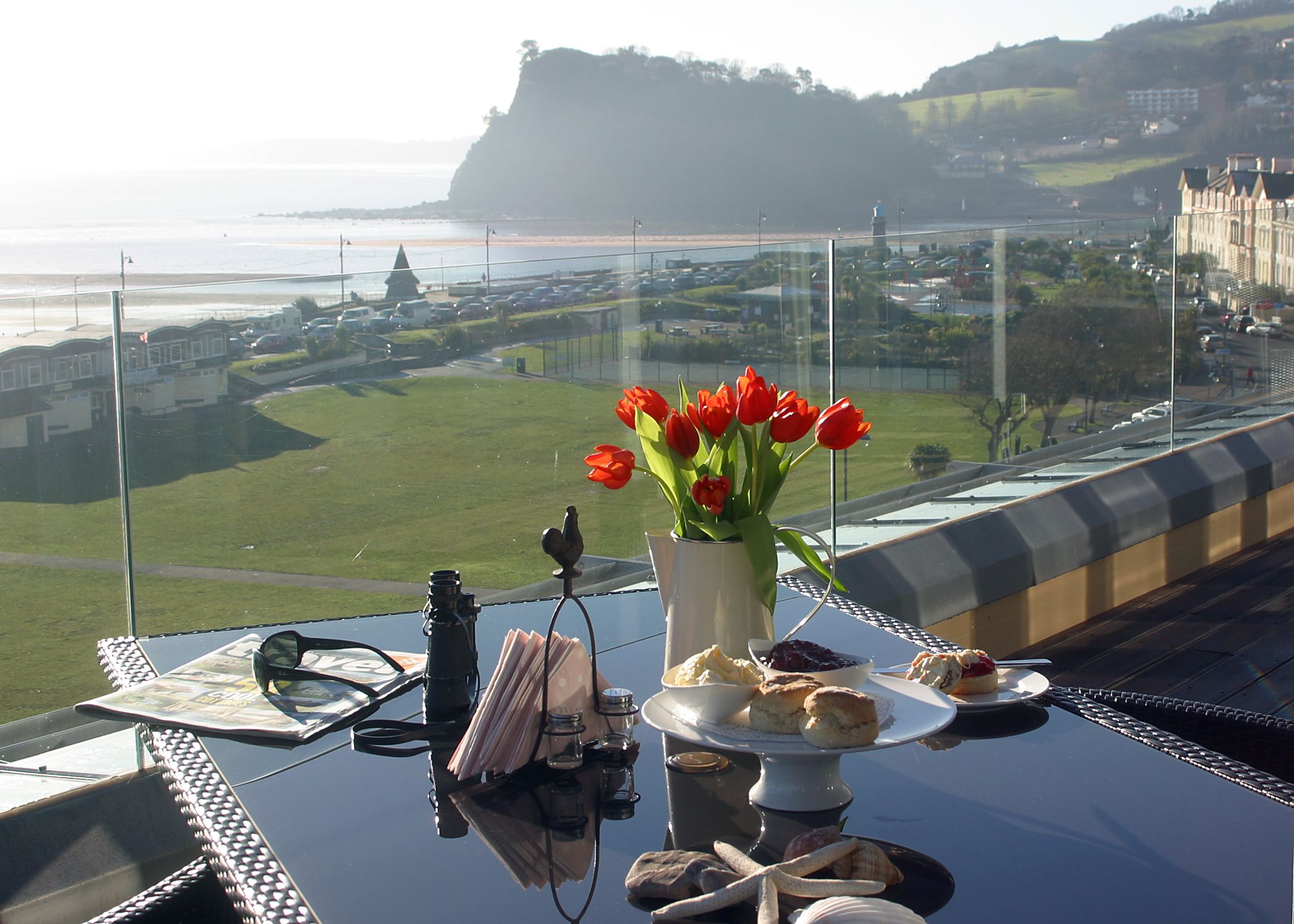 A table with a vase of red tulips, a camera, and a plate of pastries.