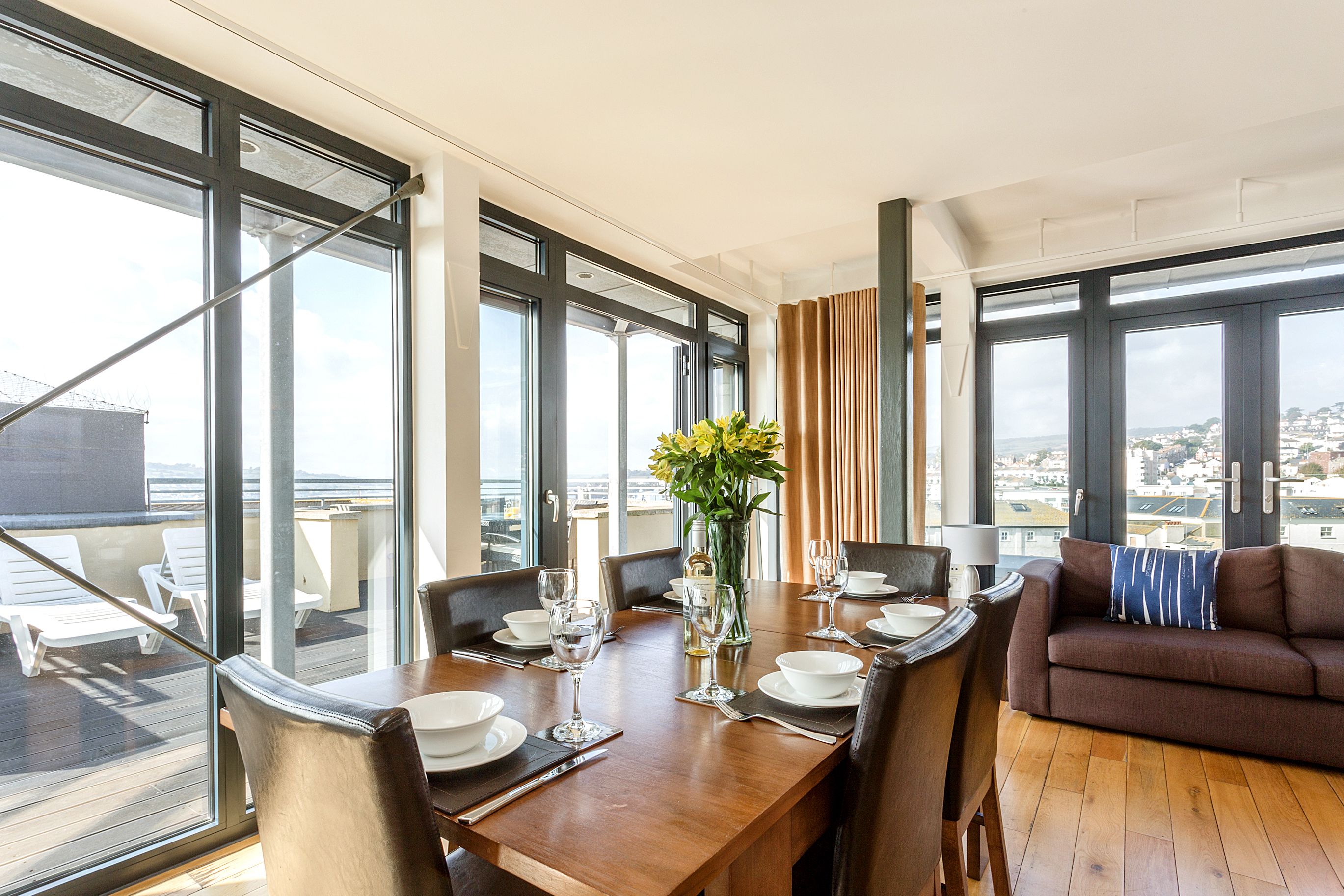 A dining area with a wooden table set for four, large windows, and a view of the city.