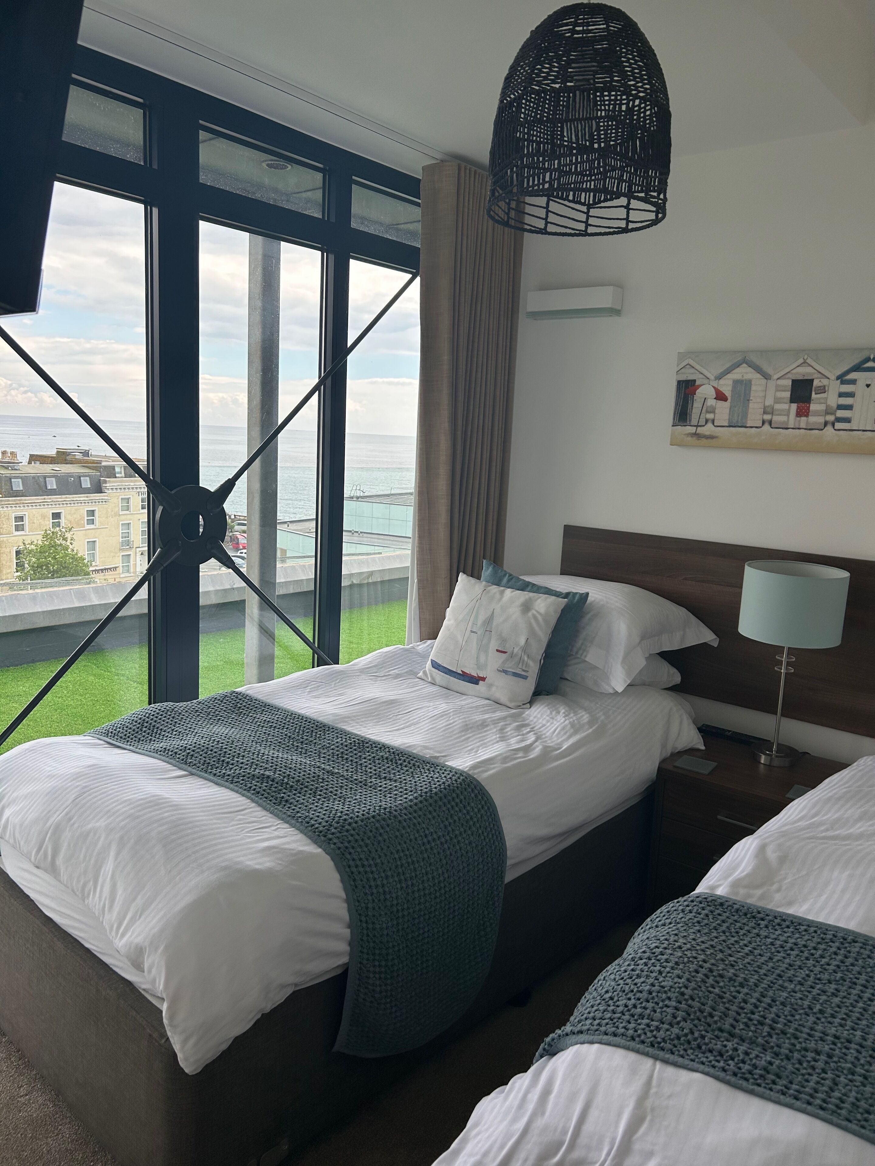Habitación de hotel con un ventanal grande que ofrece vistas a la ciudad y al mar.